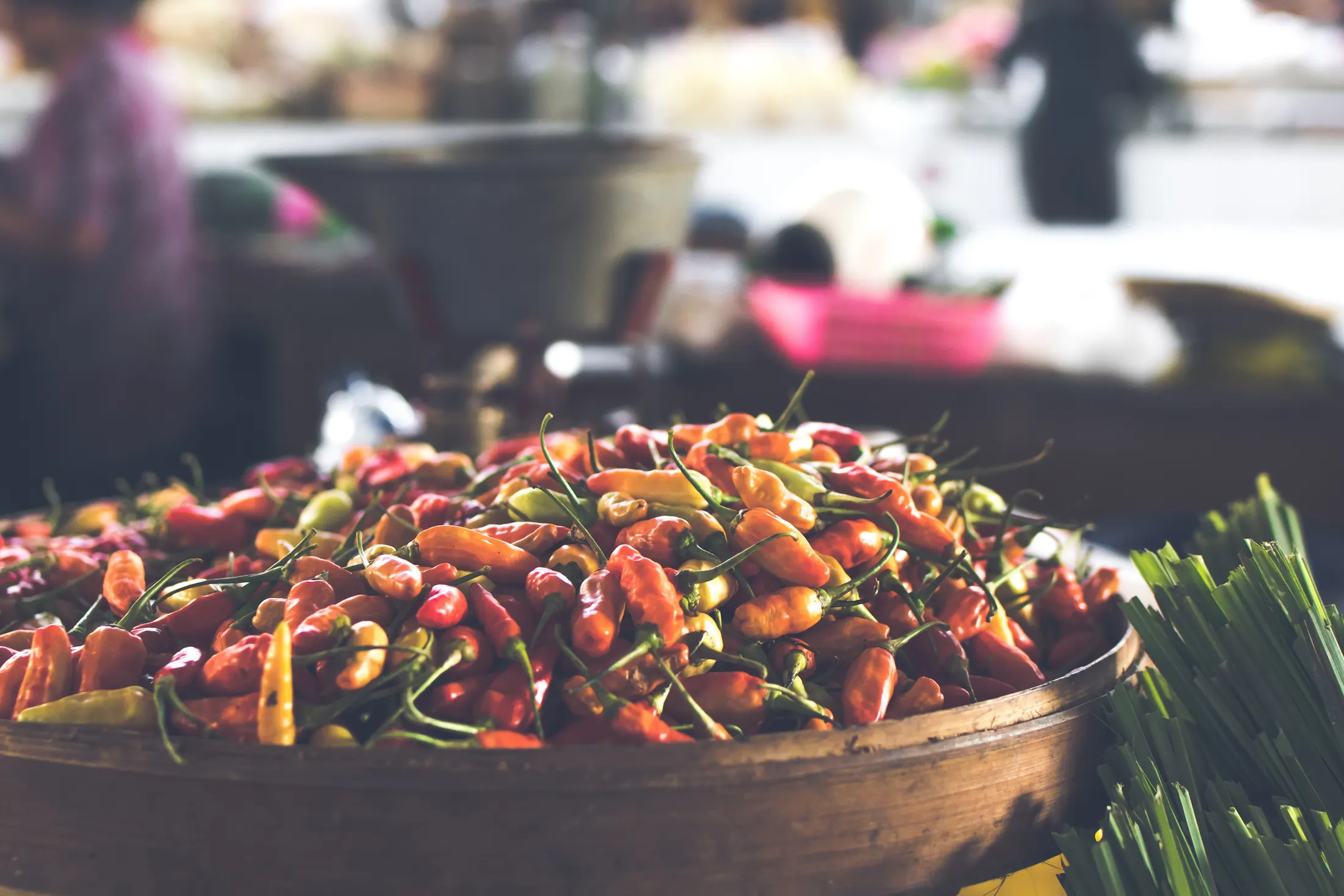 A brass bowl heaped with mixed red, orange and yellow chillies at a market stall