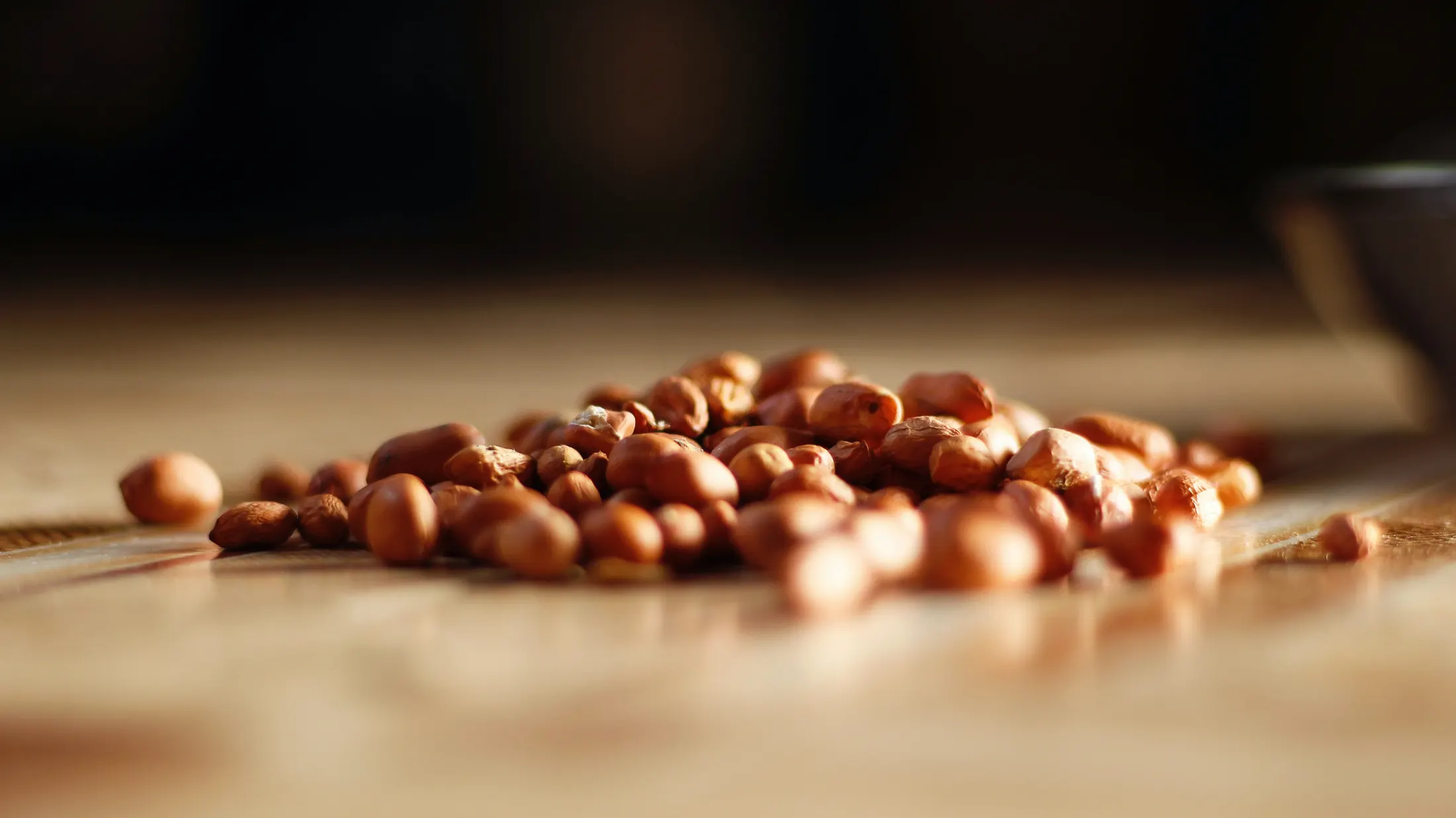 Red-skin peanuts spilled across a warm wooden surface under directional light